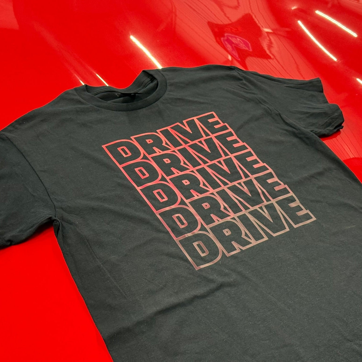 Gray t-shirt with 'DRIVE' text printed multiple times on a red surface