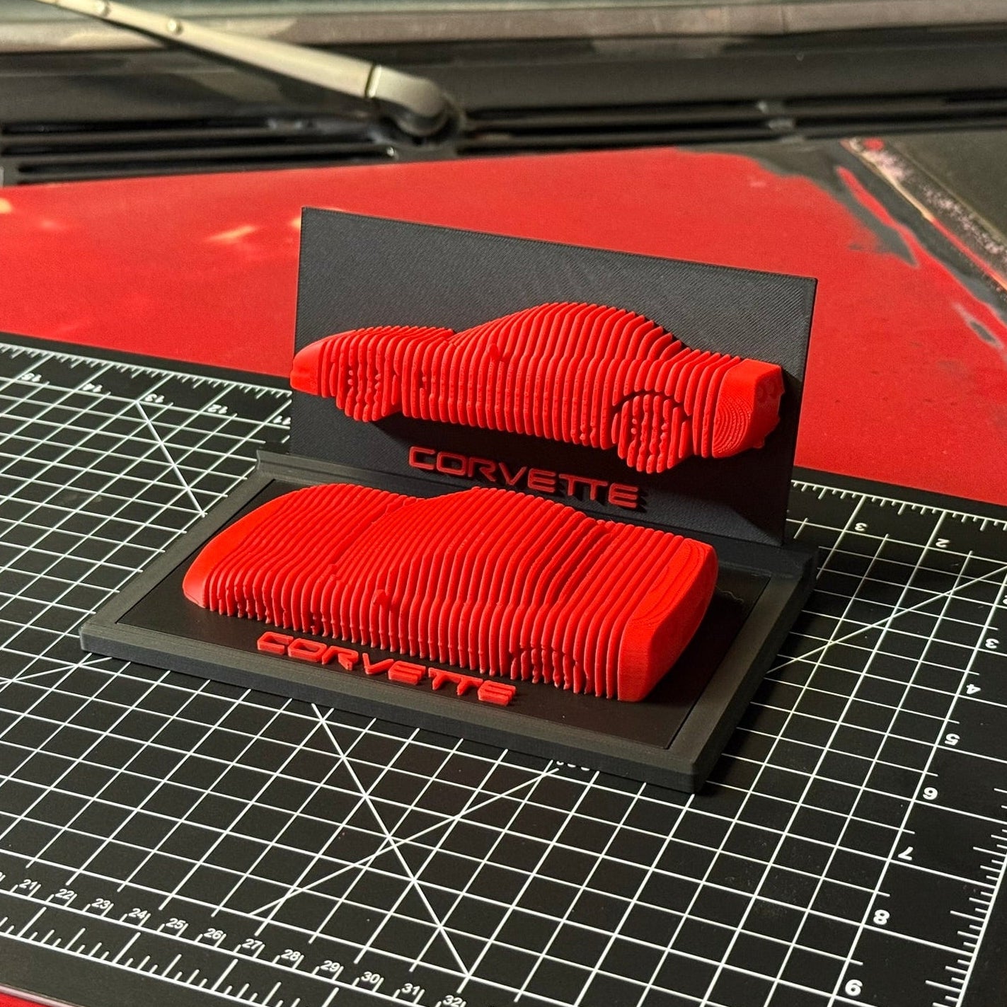 Red car parts on a black Corvette stand with a grid surface underneath
