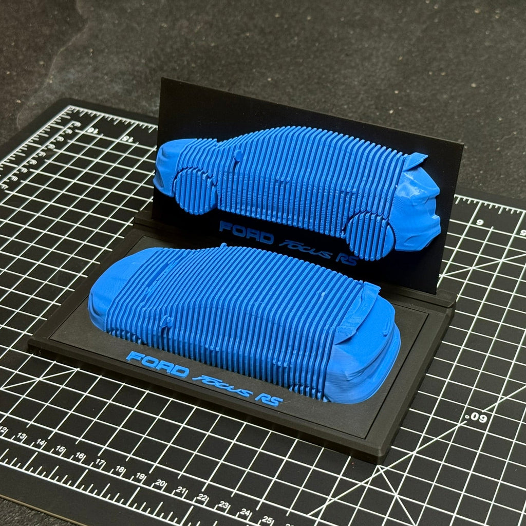 Blue 3D-printed car model on a black stand with 'Ford' branding, placed on a grid surface.