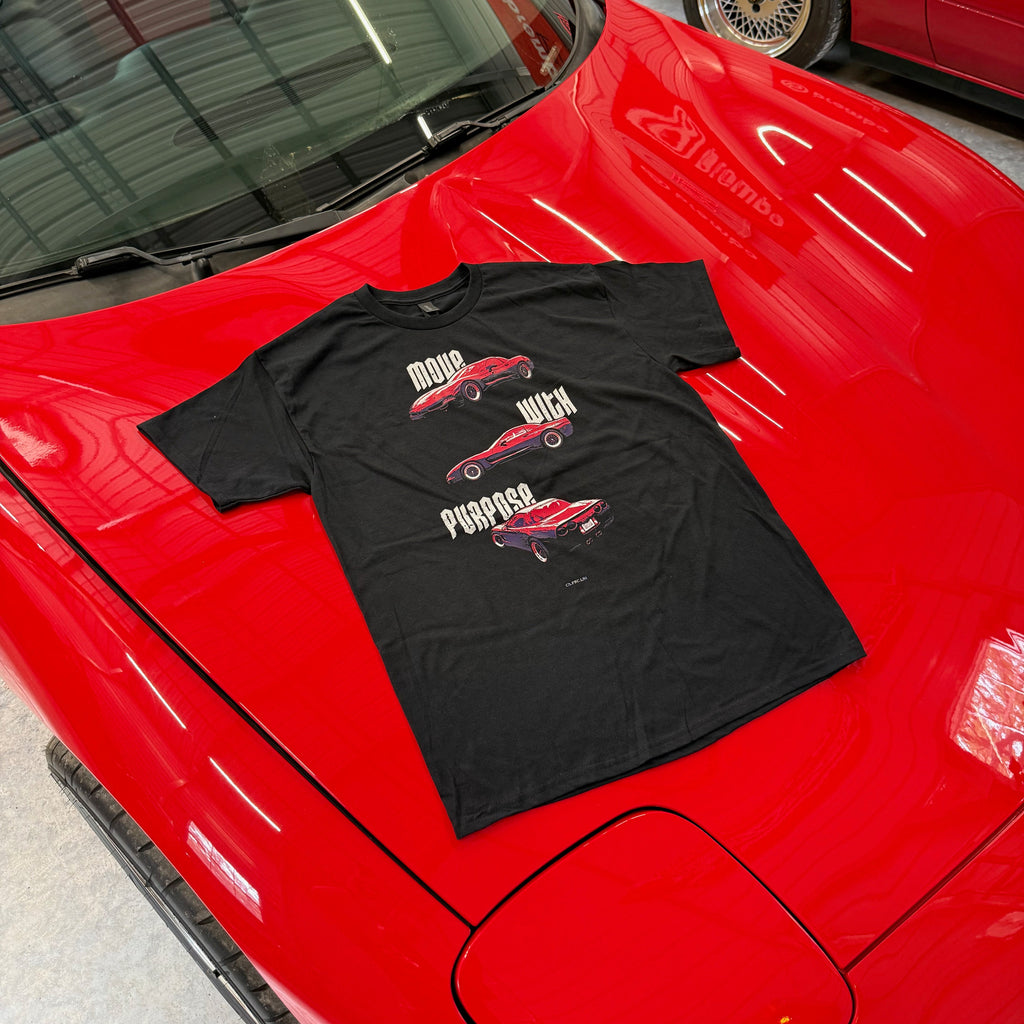 Black t-shirt with car graphics on a red car in a garage.